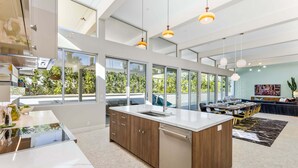 A modern kitchen with a large island, built-in appliances, and large windows offering a view of greenery. - Webb House – Mid-Century Modern in Vista Las Palma (Palm Springs)