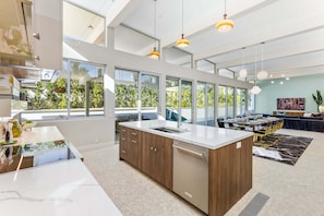 A modern kitchen with a large island, built-in appliances, and large windows offering a view of greenery.