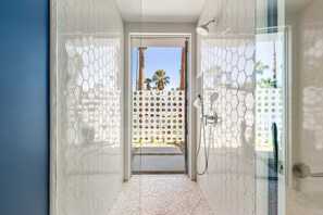 A modern bathroom with a glass door leading to a balcony with palm trees.