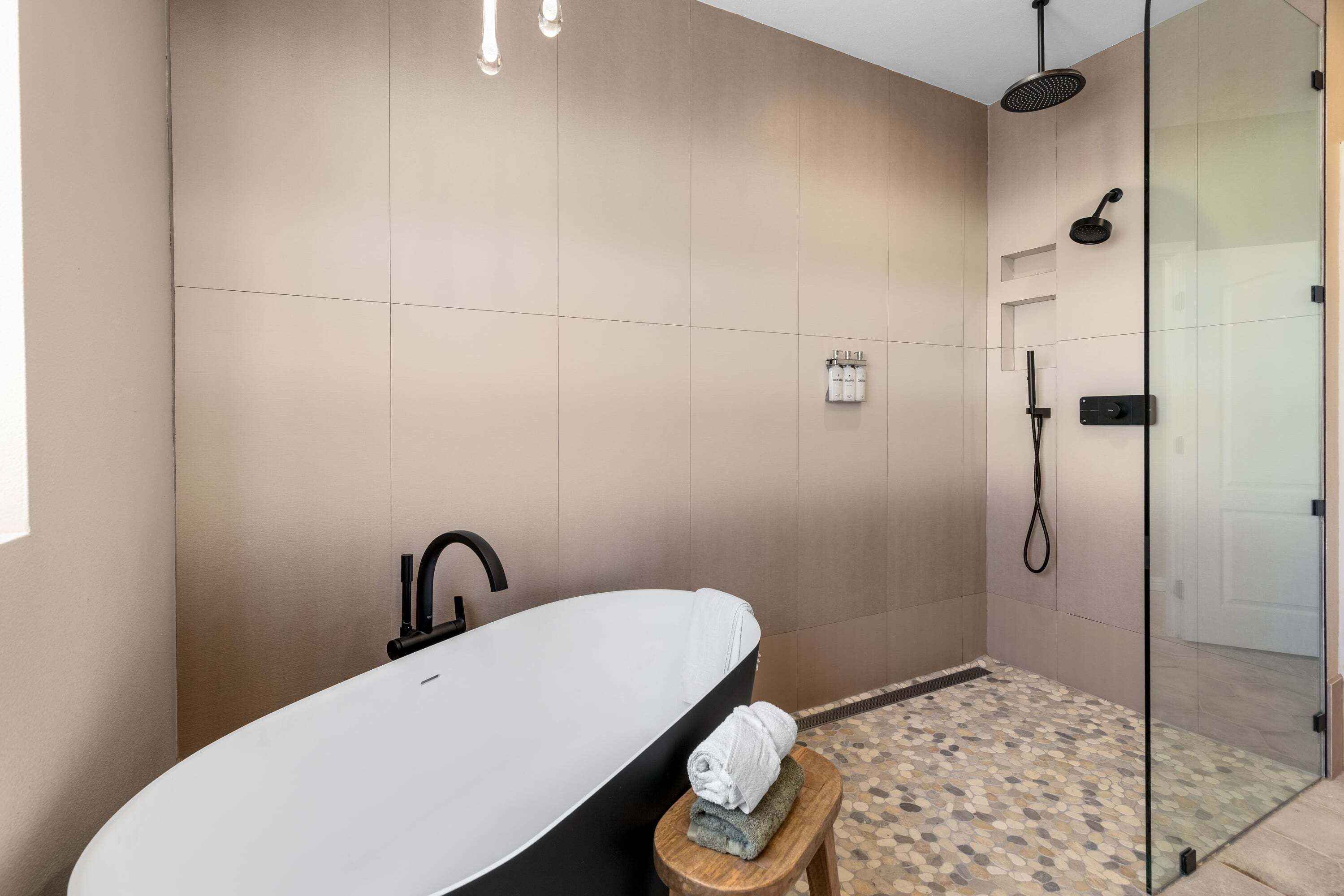 A modern bathroom with a freestanding bathtub, a glass-enclosed shower, and a small stool with towels.