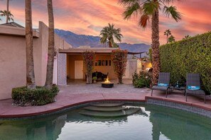 A pool area with a fire pit, outdoor seating, palm trees, and a mountain backdrop.