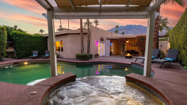 A hot tub with a waterfall effect, a pool, and a covered patio area with lounge chairs and a dining area. - Desert Delight – Palm Springs Hacienda w/ Pool & Spa (Palm Springs)
