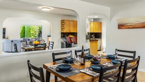 A dining area with a wooden table, chairs, and a view of a living room and kitchen. - Desert Delight – Palm Springs Hacienda w/ Pool & Spa (Palm Springs)