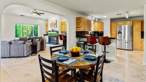 A modern kitchen with wooden cabinets, a stainless steel refrigerator, and a dining area with a round table set for four. - Desert Delight – Palm Springs Hacienda w/ Pool & Spa (Palm Springs)