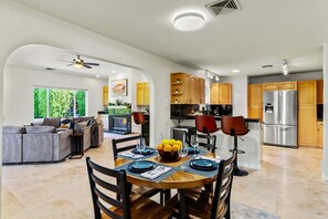 A modern kitchen with wooden cabinets, a stainless steel refrigerator, and a dining area with a round table set for four.