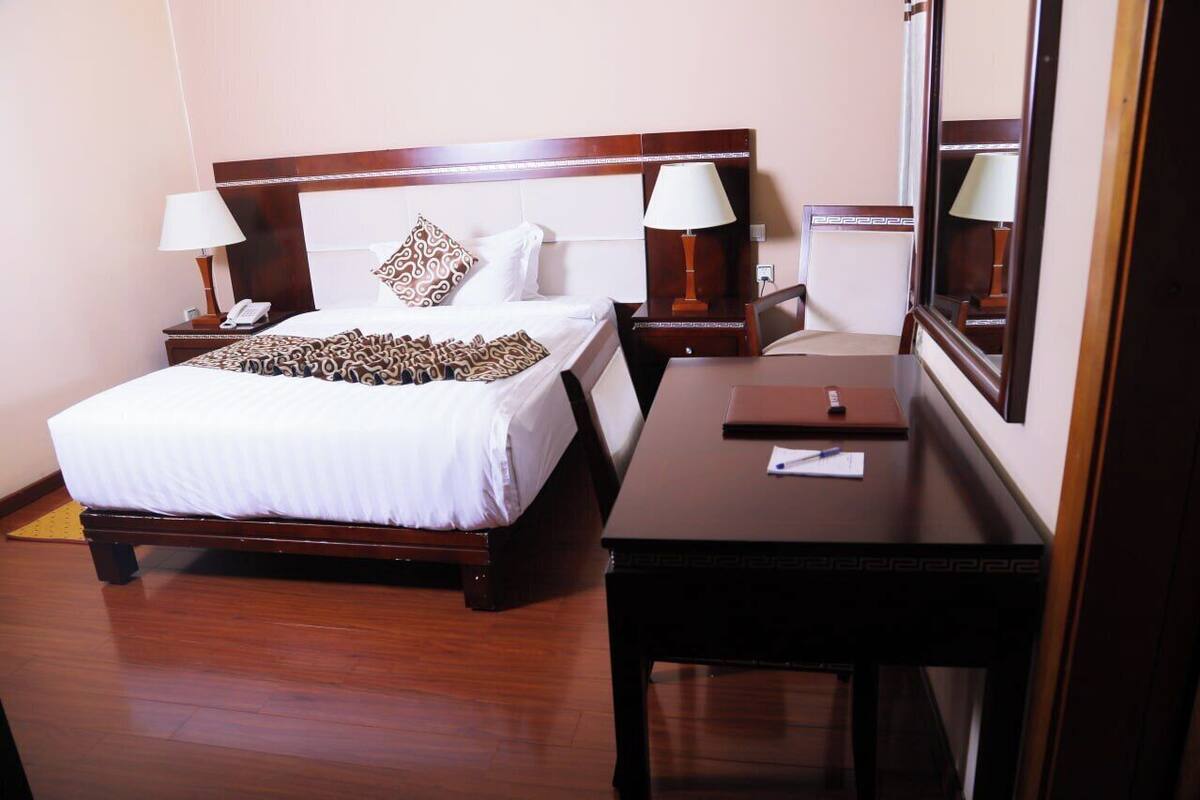 A hotel room with a wooden bed, two bedside tables with lamps, a desk, and a large mirror.
