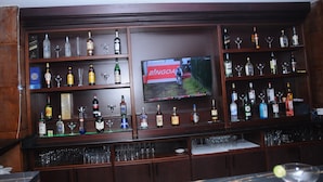 A bar area with shelves of liquor bottles and glasses, a television displaying a game, and a bar counter with glasses and a lime wedge. - Melka international hotel (Addis Ababa)