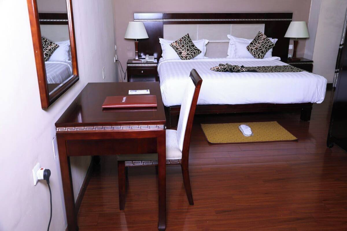 A hotel room with a bed, bedside tables, a desk, a chair, a mirror, and a bedside lamp.