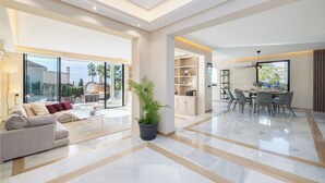 A spacious living area with a sofa, coffee table, and potted plant. There is a dining area with chairs and a table. The room has large windows and a view of the outside. - Villa El Paraiso Marbella- 4 Bedrooms (5-Beds) (Benahavís)