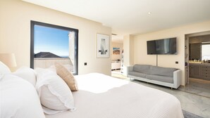 A modern bedroom with a large bed, a grey sofa, a flat-screen TV, and a view of the outdoors. - Villa El Paraiso Marbella- 4 Bedrooms (5-Beds) (Benahavís)