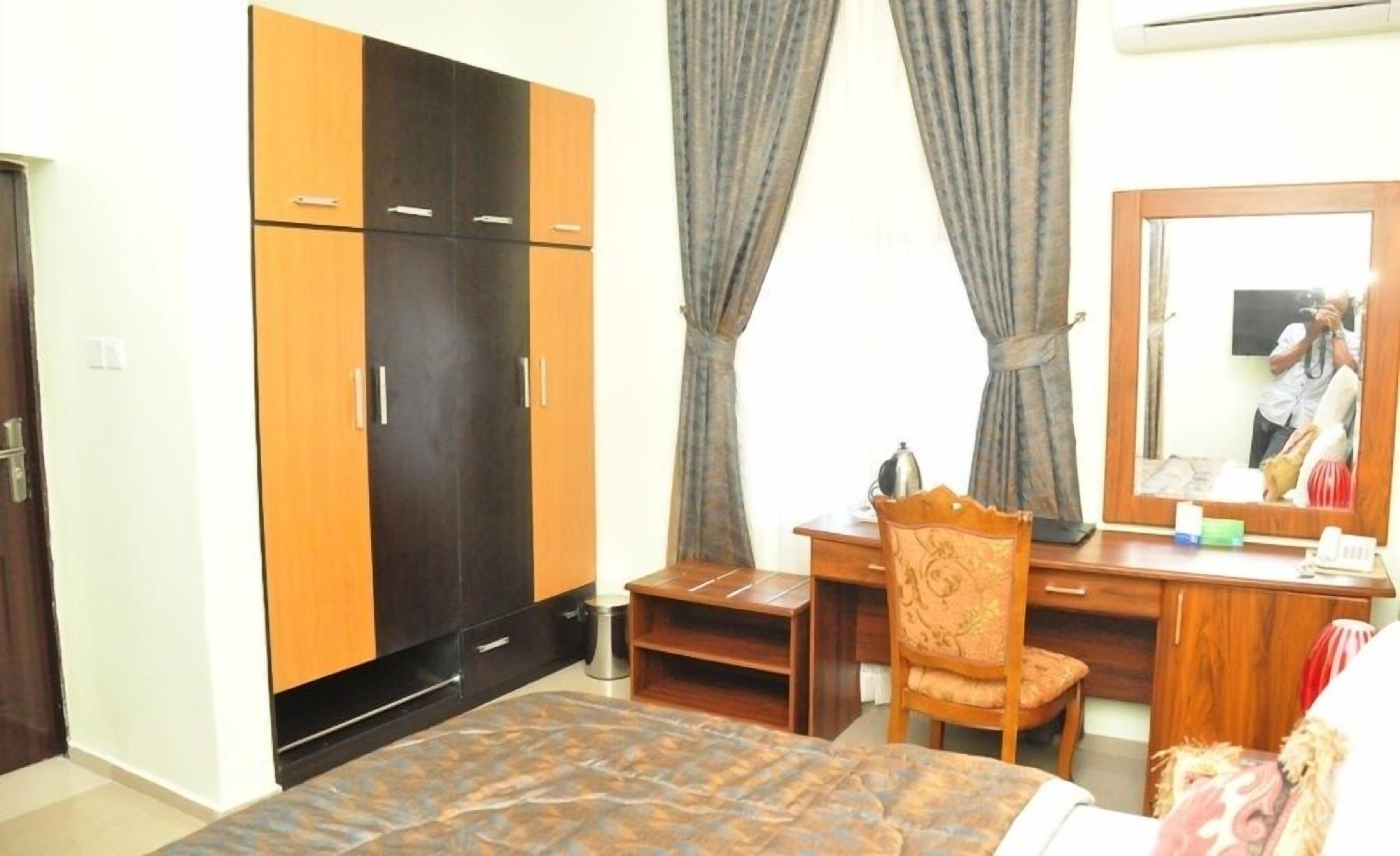 A bedroom with a bed, a desk, a chair, a wardrobe, and a mirror.