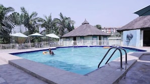 Uma piscina com estrutura de palha, palmeiras e guarda-sóis.