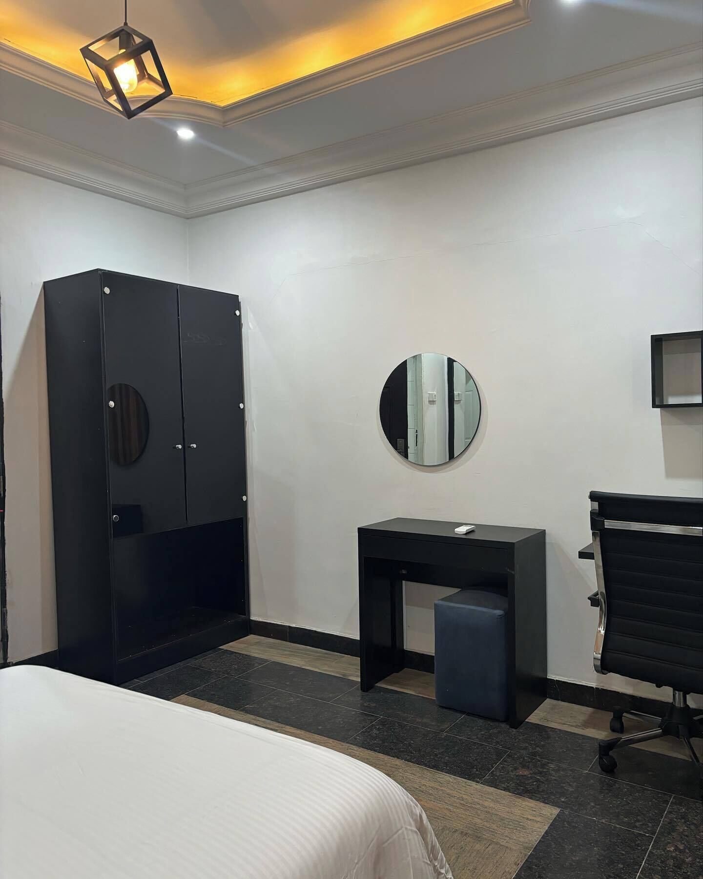 A hotel room with a bed, a desk, a chair, a wardrobe, and a round mirror.