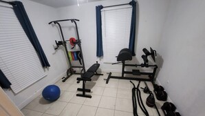Une petite pièce bien éclairée, équipée d’un banc, d’un banc de musculation et de ballons d’exercice.
