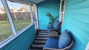 Une véranda à l’extérieur bleu, des fauteuils en osier avec des coussins et une vue sur le jardin arrière.