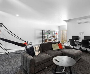 A modern living room with a sectional sofa, a small round coffee table, a bookshelf, and a gaming setup. - Stylish Home with Rumpus Room (Cowes)