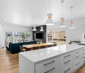 Une cuisine moderne dotée d’un grand îlot central, de luminaires suspendus et d’un coin repas avec un canapé et des chaises.