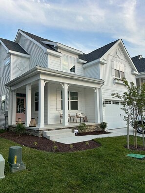 Ein zweigeschossiges Haus mit überdachter Veranda, Garage und gepflegtem Rasen.