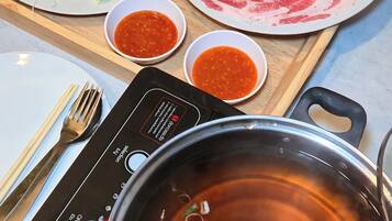 Uma mesa com um prato de carne crua, um prato de legumes, duas pequenas tigelas de molho, hashis, um garfo e um fogão elétrico portátil com uma panela de água fervente.
