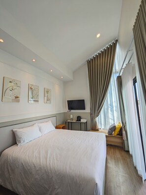Ein Hotelzimmer mit einem großen Bett, einem flachbildfernseher an der Wand, einem kleinen Tisch mit Lampe und einem Fenster mit Vorhängen.