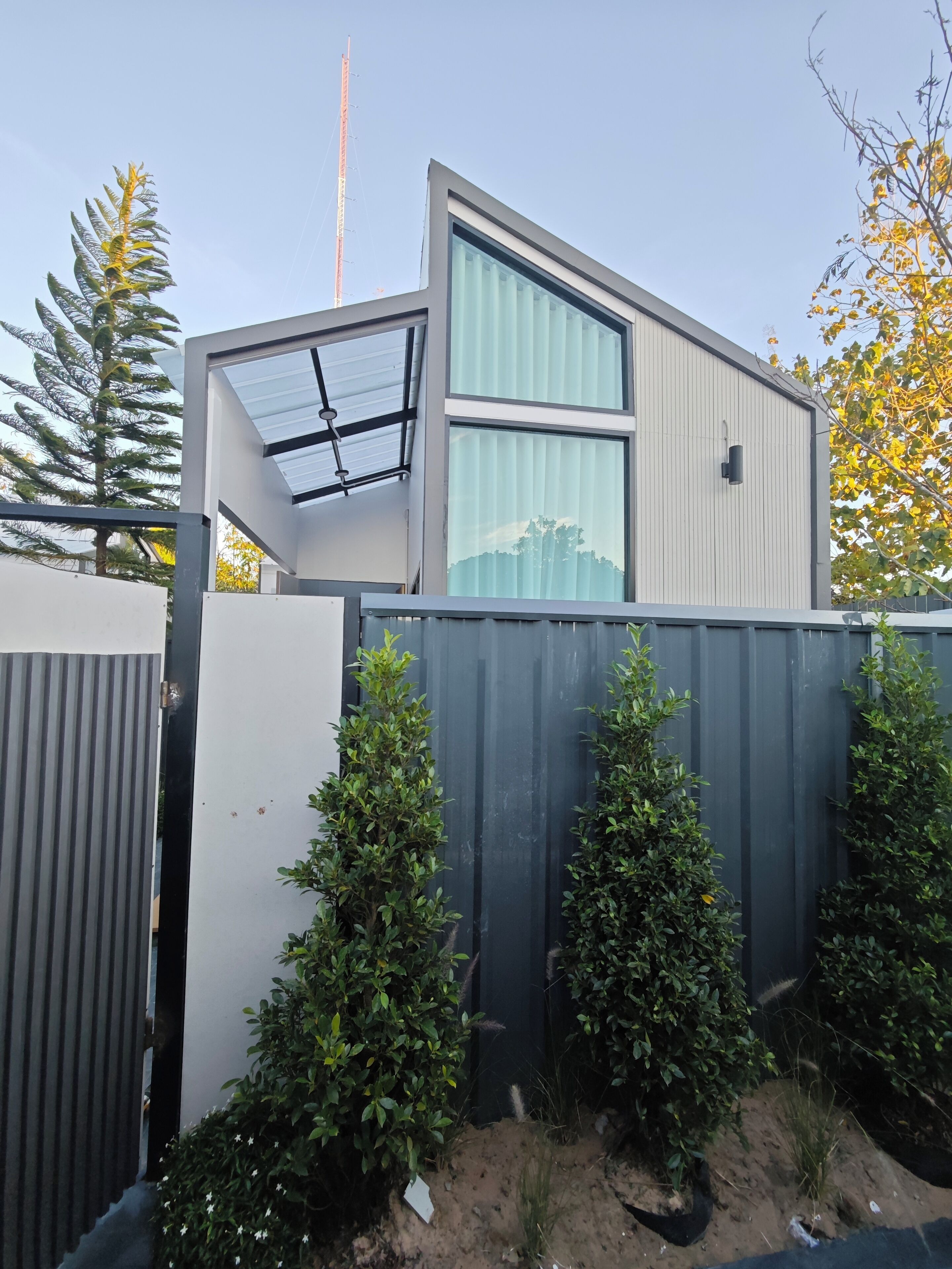 A modern, compact building with a flat roof, large windows, and a metal fence surrounding the property.