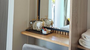 A hotel room with a vanity area, a mirror, a desk with a tray holding cups and glasses, and a chair. - S'Villa  (Warin Chamrap)