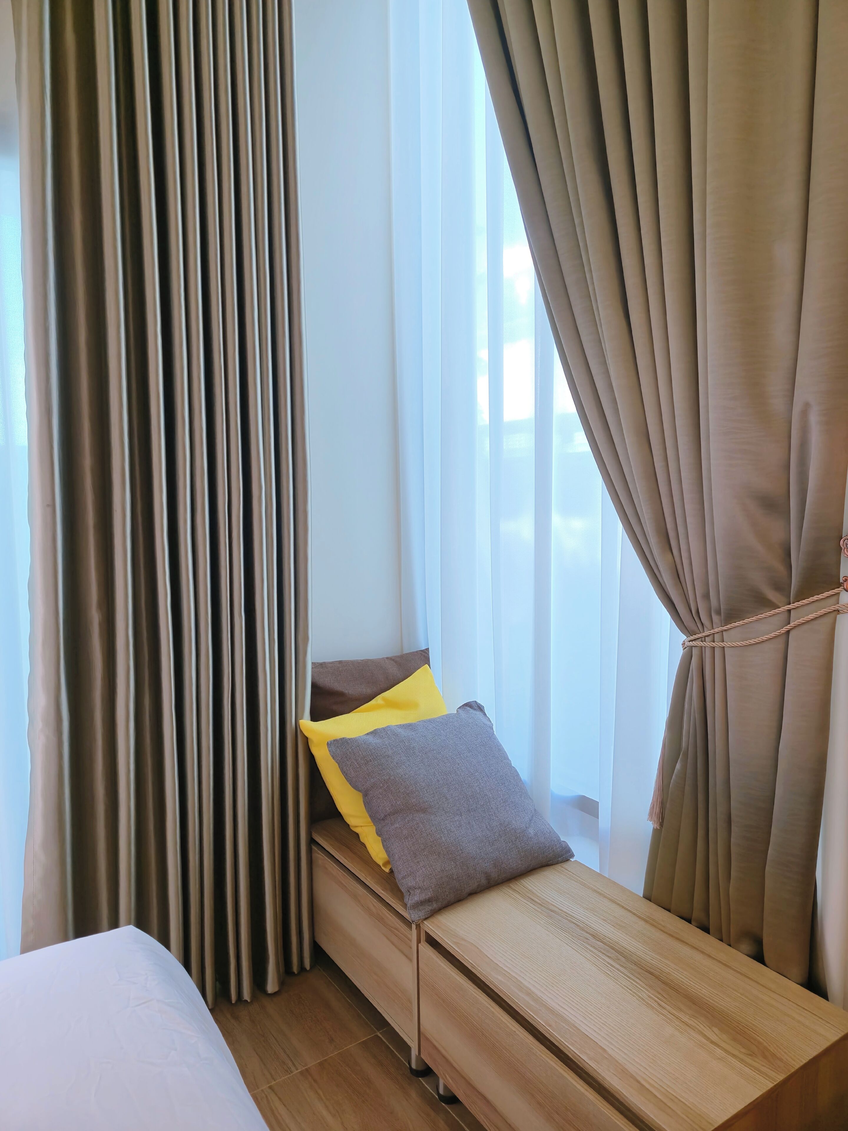 A hotel room with a bed, a wooden bench, and curtains.