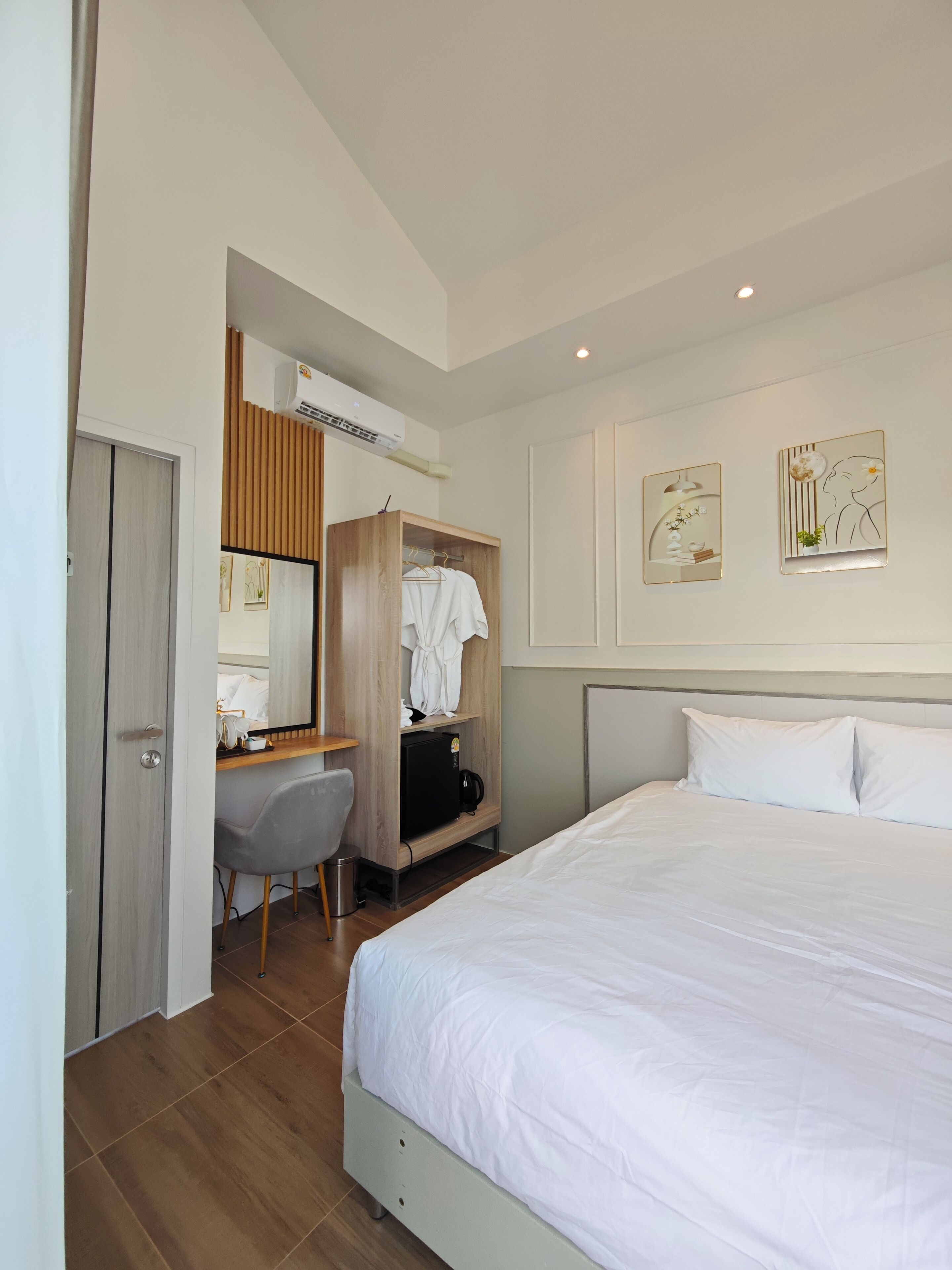A hotel room with a bed, a desk with a chair, a wardrobe, and two wall art pieces.