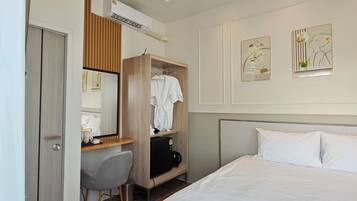 A hotel room with a bed, a desk with a chair, a wardrobe, and two wall art pieces.