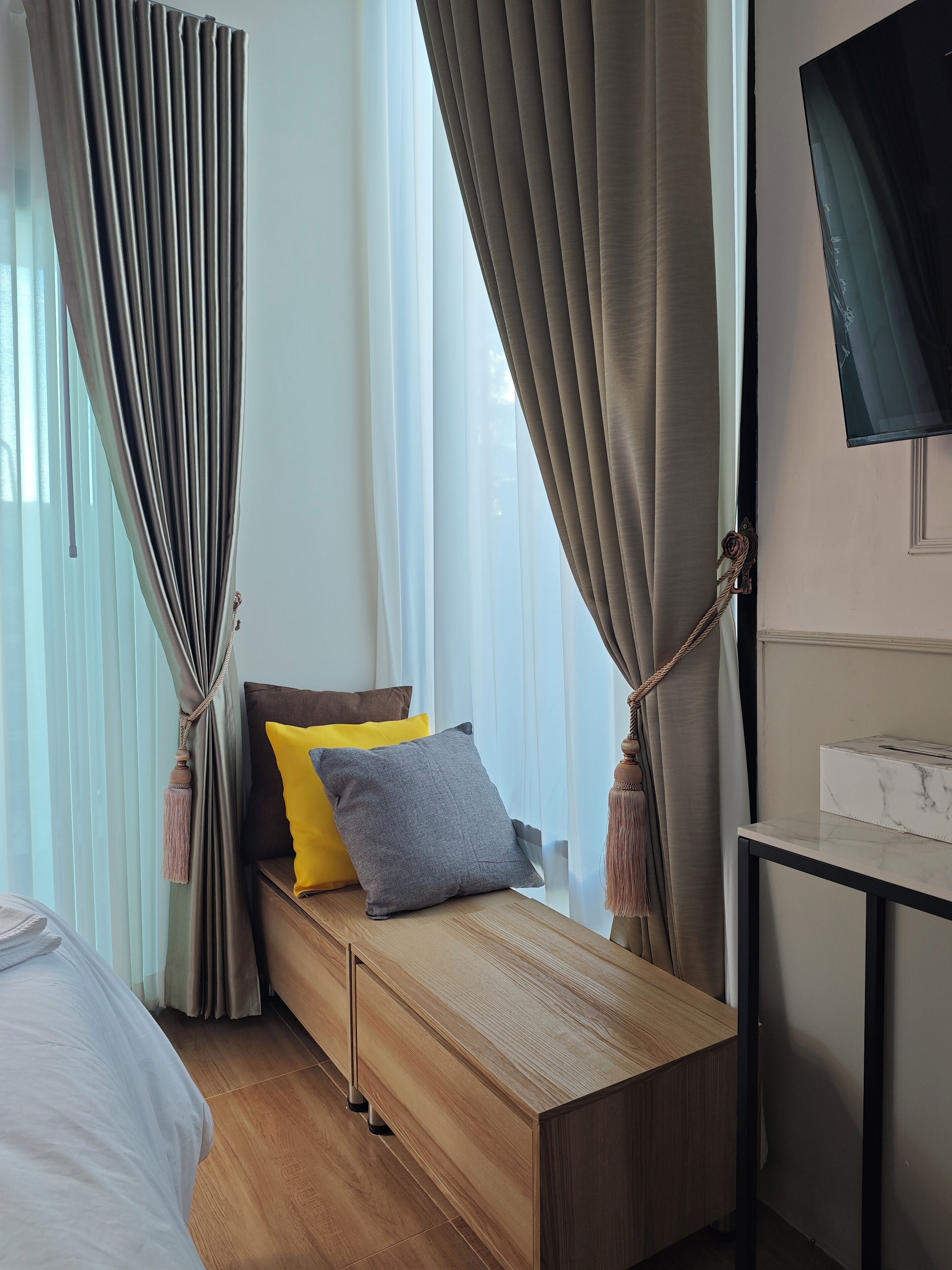 A modern bedroom with a wooden bed, a bedside table, a TV, and curtains.