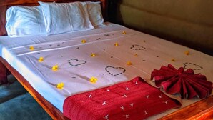 Ein Bett mit weißer Bettdecke, gelben Blumen, roten Herzchen und einem roten Handtuch.