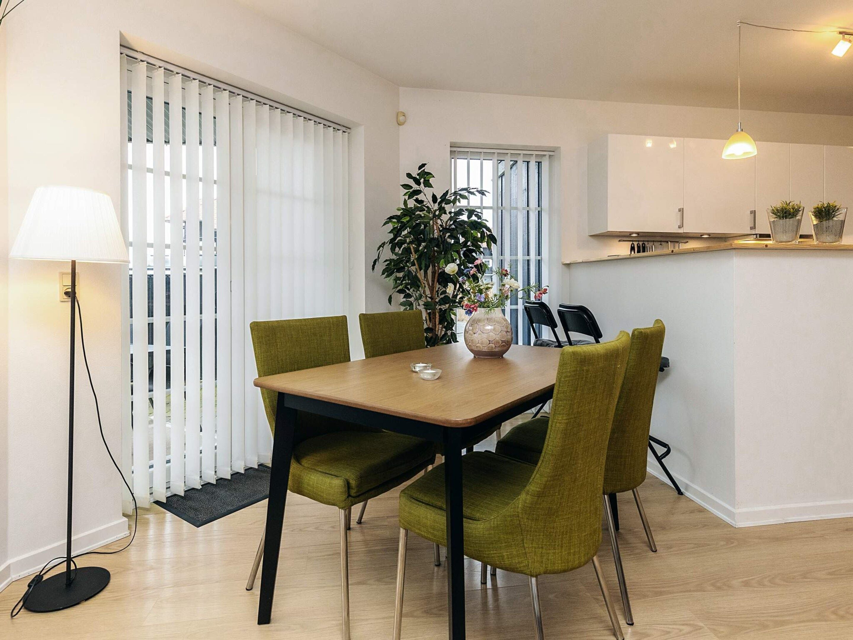 Uma área de refeições com mesa de madeira, cadeiras estofadas em verde e um vaso com planta.