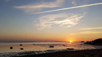 A sunset over a calm sea with boats and a clear sky.