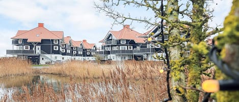 A row of traditional houses with red roofs, a calm water body in the foreground, and a clear sky.