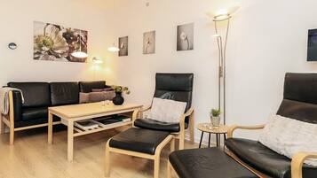 Een moderne woonkamer met een bank, twee fauteuils, een salontafel en een vloerlamp.