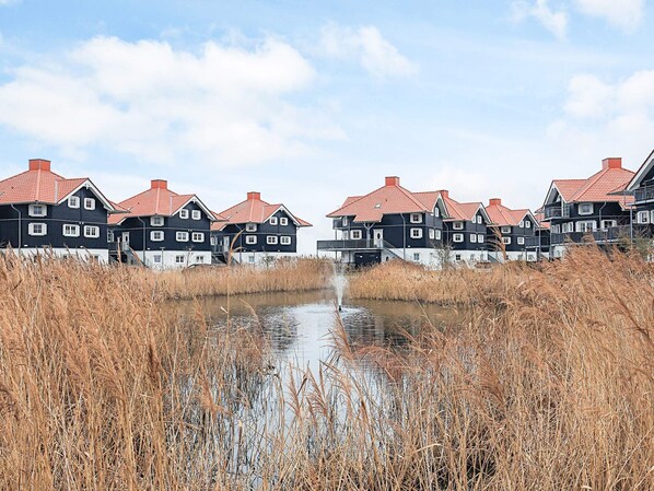 A row of black and white houses with red roofs, a canal in the foreground, and tall reeds.