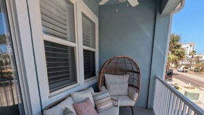 Ein Balkon mit Deckenventilator, einem Korbstuhl, einer gepolsterten Bank und einem Geländer.