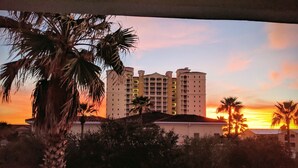 Ein Hotel mit mehreren Stockwerken, umgeben von Palmen und einem Sonnenuntergang im Hintergrund.