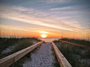 A wooden pathway leading to the beach with a sunset in the background.