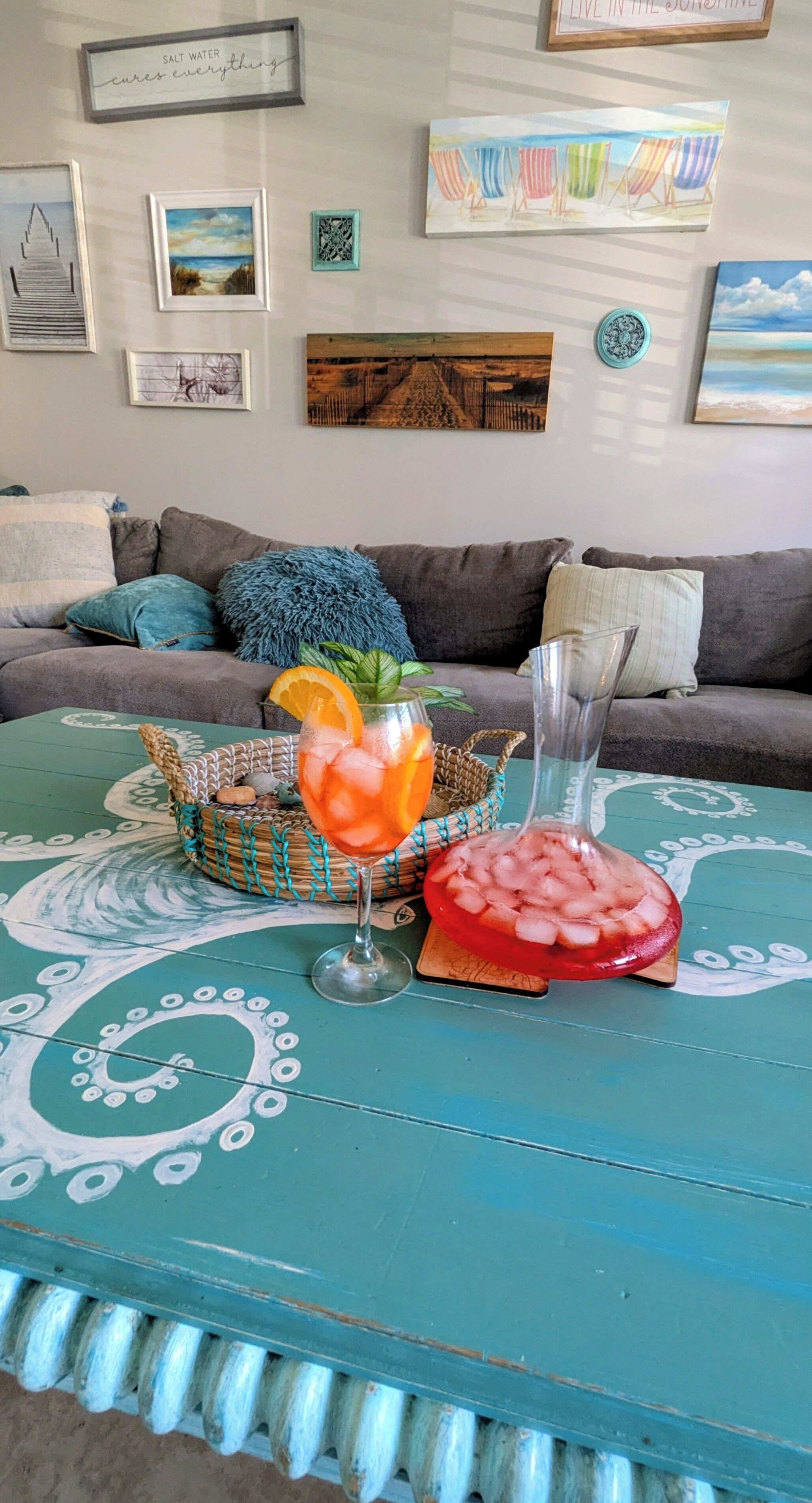 A living room with a teal coffee table, a glass of iced drink with an orange slice, and a decorative bowl.