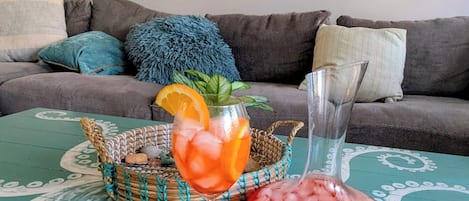 A living room with a teal coffee table, a glass of iced drink with an orange slice, and a decorative bowl.