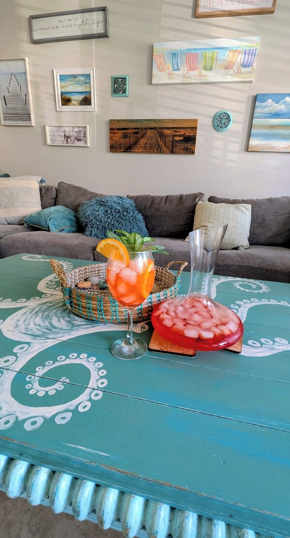 A living room with a teal coffee table, a glass of iced drink with an orange slice, and a decorative bowl.