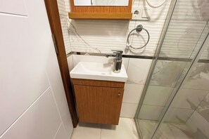 Ein Badezimmer mit weißem Waschbecken, Holzschrank und einer Duschkabine aus Glas.