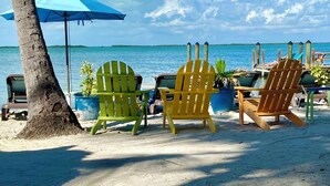 A beach scene with colorful Adirondack chairs, a blue umbrella, and a view of the ocean. - Seafarer Key Largo (Key Largo)