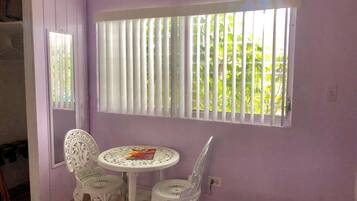 A room with a purple wall, a window with vertical blinds, a round table with two chairs, and a mirror on the wall.