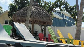 Beach chairs and a thatched umbrella in a sunny outdoor area with a building in the background.