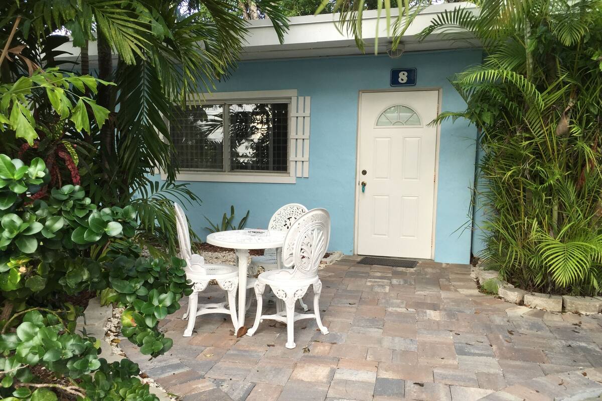A patio with a white table and chairs, a white door, and a blue wall with the number 8.