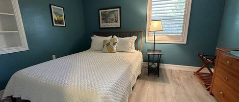 A bedroom with a bed, a nightstand, a lamp, and a dresser.