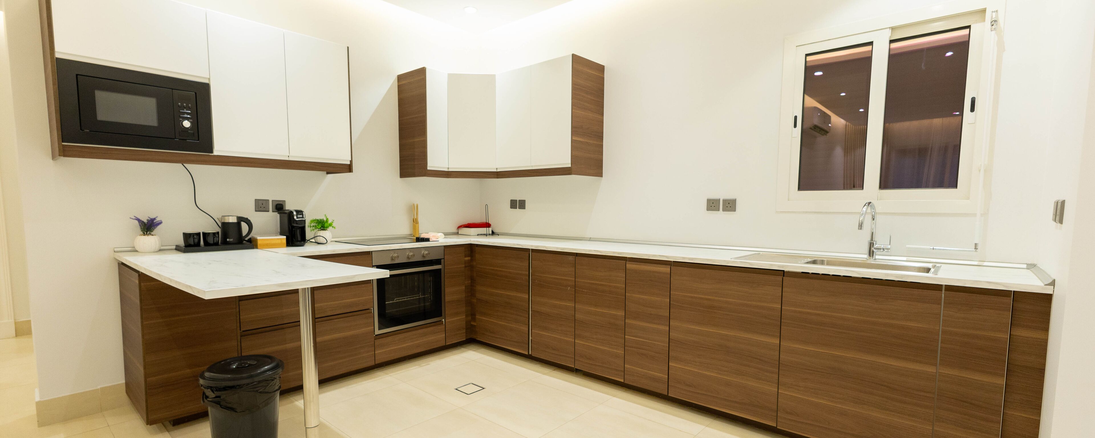 A modern kitchen with wooden cabinets, a built-in oven, a microwave, and a window with curtains.