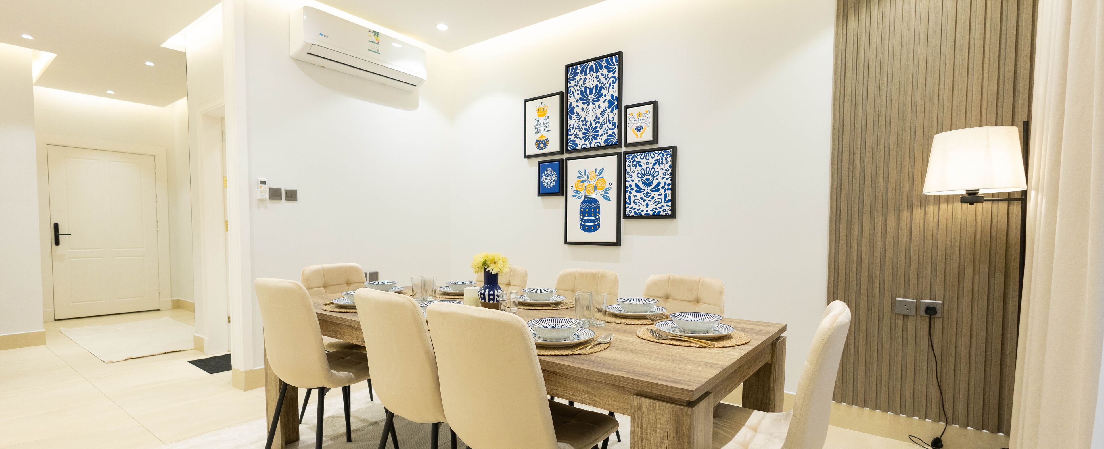 A dining area with a wooden table, beige chairs, and framed artwork on the wall.